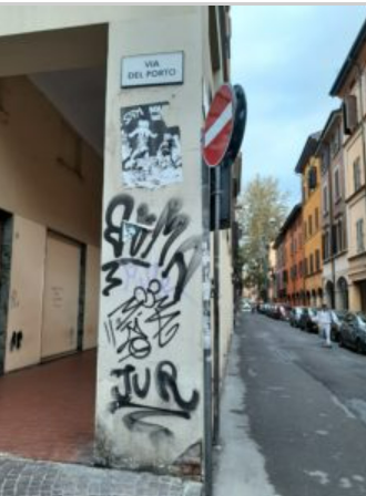 foto delmuro giallo con tante scritte nere a spray e la targa della via del porto